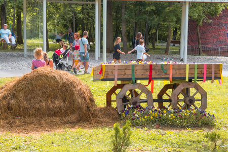 Children playing near a haystack and decorated flower cart at an outdoor festival with people in the background.の写真素材