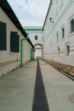 A narrow walkway at New Jerusalem Monastery, bordered by white brick walls and cobblestones. The path features a green drainpipe and leads to a distant archway, evoking a tranquil, historical settingの写真素材
