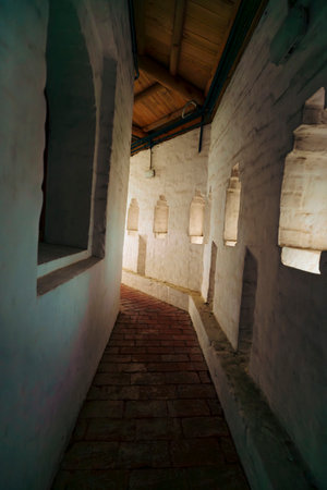 A narrow corridor in a historical building, dimly lit by small windows along the wall, creating a mysterious and ancient ambiance.の写真素材