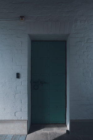 A closed metal door in a dimly lit corridor with brick walls, evoking a sense of mystery and solitude.の写真素材