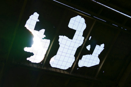 A damaged ceiling with holes revealing the blue sky and protective netting, indicating neglect and deterioration.の写真素材