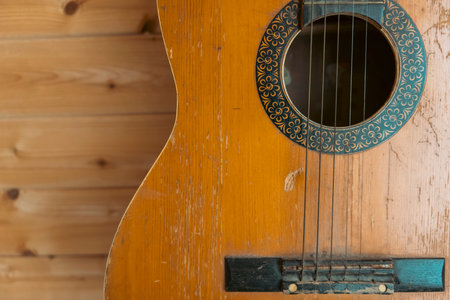 An old, well-worn acoustic guitar with visible scratches and marks, hanging on a wooden wall.The...