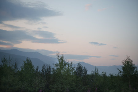 A tranquil scene of misty mountains and green fields at dawn, with a soft pastel sky overhead, creating a serene and peaceful atmosphere.の写真素材