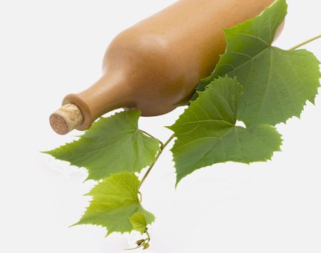 Ceramic bottle of wine with grapes leaves lies isolated on white backgroundの写真素材