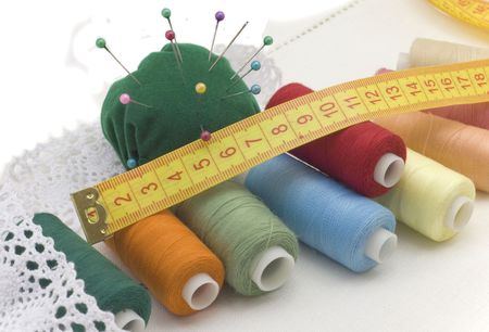 Multi-coloured threads for sewing, needles, a measuring tape on a white canvas