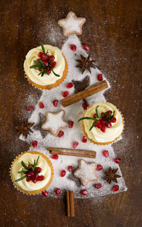 Christmas cupcakes with vanilla frosting, cranberries and rosemary on wooden backgroundの写真素材
