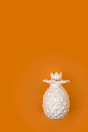 Decorative ceramic white pineapple on a bright orange background. Pineapple on an orange backgroundの写真素材