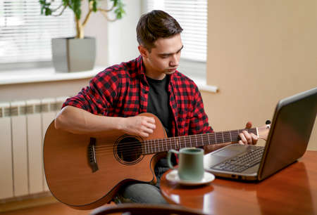 Man on kitchen playing the guitar with laptop at homeの写真素材
