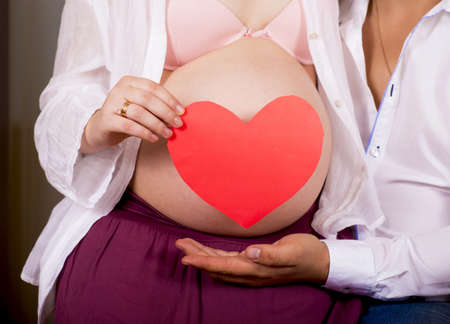A pregnant woman is holding a heart-shaped paper on her abdomenの写真素材