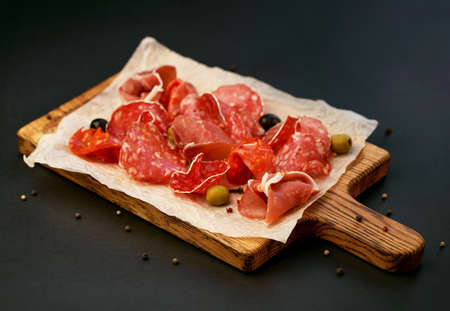 cold cuts - jamon, ham, salami on a wooden board on a black backgroundの写真素材