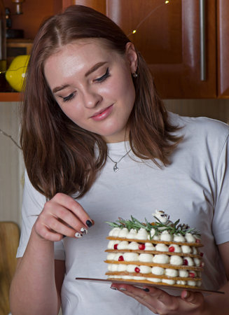 Young blonde girl in her kitchen holding a Christmas cake enjoying the smell