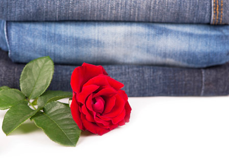 jeans clothes are put by a pile and a red rose on a white backgroundの写真素材