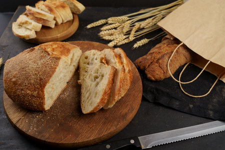 Concept of homemade bread, natural farm products, domestic production. Healthy and tasty organic food. Round loaf of freshly baked sourdough bread with knife on cutting board. Fresh bread slice and cutting knife on rustic tableの写真素材