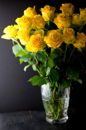 bouquet of beautiful yellow roses with leaves in a vintage crystal vase on a blackの写真素材