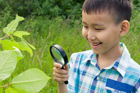 Boy with magnifying glass outdoors.The concept of childhood, nature research, search and discovery, science and knowledge in biology and botany. A child of Asian appearance.の写真素材