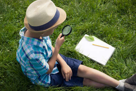 A boy holding a magnifier and studying outside. The concept of homeschooling, 
search and discovery, science and knowledge in biology and botany, nature research.  A child of Asian appearance. Image.の写真素材