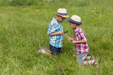 Two boys with magnifying glass outdoors. The concept of friendship of children, brothers, nature research, search and discovery, science and knowledge in biology and botany. Asian children. Image.の写真素材