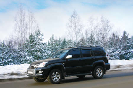  black off-road car goes on highway along wood.の写真素材