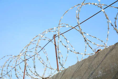 Barbed wire over concrete fence against the skyの写真素材