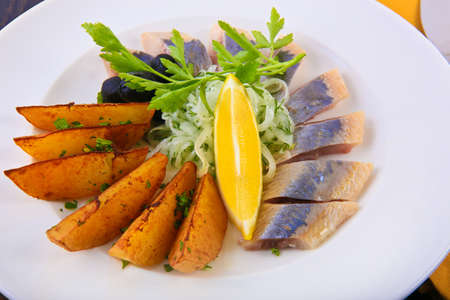 herring with baked potato onions and olives on white plateの写真素材