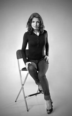 beautiful brunette in jeans sitting on high chair monochromeの写真素材
