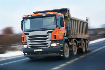 dump truck with an orange cabin goes on the highway in the winterの写真素材