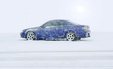 blue car in the winter on snow under snowfallの写真素材