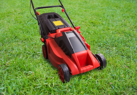 Red electric lawn mower on green lawnの写真素材