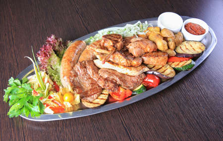 meat allsorts with vegetables in oval metal plate on tableの写真素材