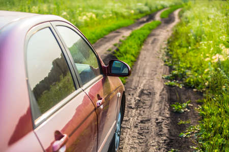 red car on country road on summer meadowの写真素材