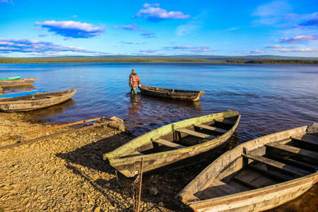 fisherman walking in the water with a boat along the shore of the lakeの写真素材