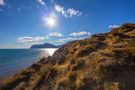Steep grassy slope. Sea and mountains in the background.の写真素材