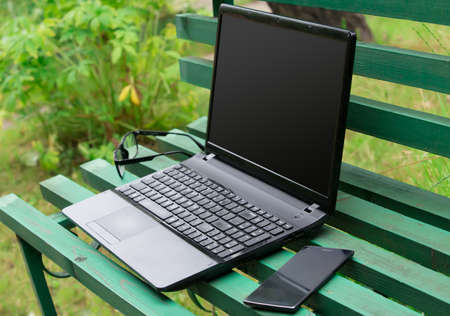 Laptop, smartphone and glasses on a park benchの写真素材