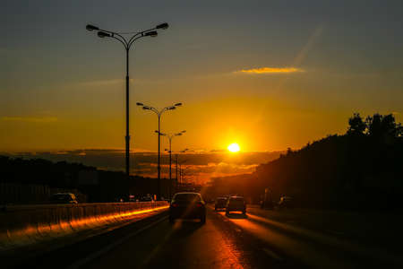 Cars move along the road at the last rays of setting sun.の写真素材