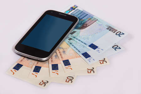 Mobile phone lies on Euro banknotes. Close-up. Isolated.