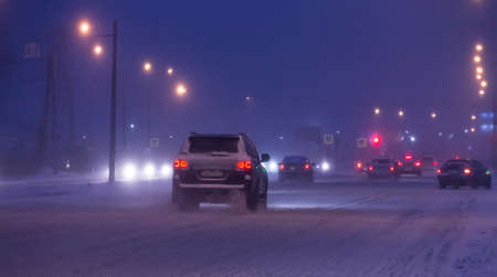 Cars drive along snow-covered road at night in winter.の写真素材