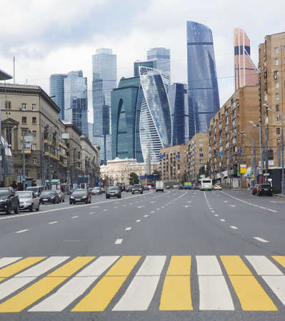 Cars move on the road along the street with classic style houses and skyscrapers in the background.の写真素材