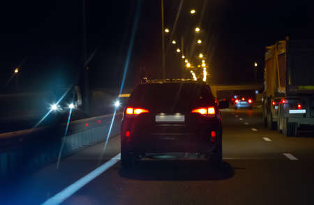 Cars with lights on move on wide multi-lane road at night. Back view.の写真素材