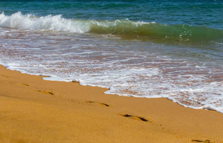 Sea waves roll on to shore. Sea foam. Traces of human feet. Closeup.の写真素材