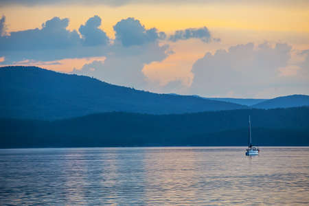 yacht on the lake in the evening against the background of mountains and beautiful sunsetの写真素材