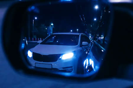 Reflection of overtaking car in rearview mirror. Dark night. Blurred background.