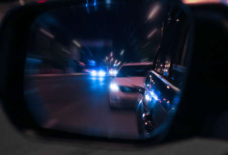 Reflection of moving cars in rearview mirror. Dark night. Blurred background.の写真素材