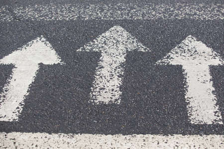 Three white arrows pointing in one direction on gray asphalt floor. Walking direction, crossroads, intersection, crosswayの写真素材