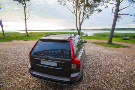 Car on the shore of a picturesque lake with trees in the background.