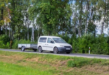 Car with a Trailer moves on a country road in the summer