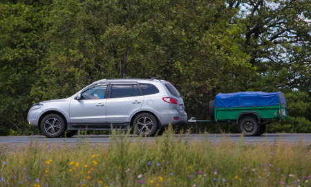 Car with a Trailer moves on a country road in the summer