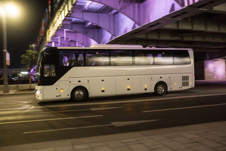 Bus moves on dark city street at night. Blurred background.