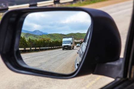 View through the rearview mirror of the car on the movement of cars on a country highway