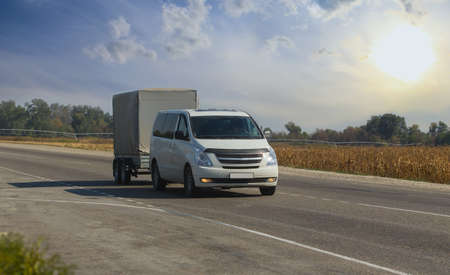 Minivan with trailer. Moving along a suburban highway at dawn.