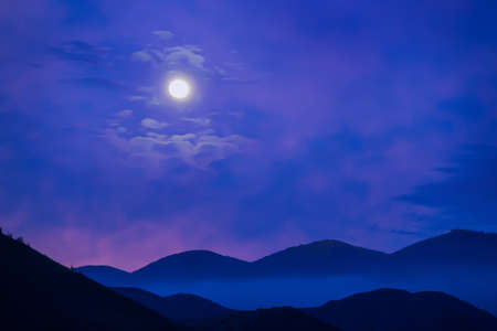 Moonlit night over the mountains in the fog